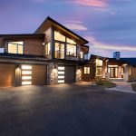 Modern luxury house with illuminated garage doors at sunset.