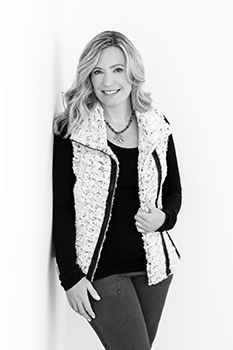 Smiling woman in a black top and patterned vest posing against a white background.